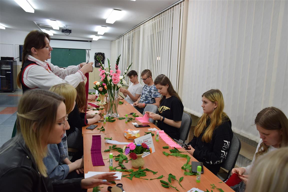 Prowadząca pokazuje młodzieży jak wykonać płatki róży do kwiatów z bibyły