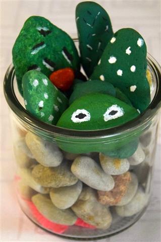 Szklana doniczka, w której znajdują się kamienie koloru szarego, czerwonego, kamienie pomalowane na zielono w białe kropki oraz żabkę