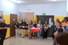 Wychowawca przemawia do grupy młodzieży pośród której dwie dziewczyny trzymają wielkie serce wypełnione kartami 