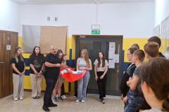 Wychowawca przemawia do grupy młodzieży pośród której dwie dziewczyny trzymają wielkie serce wypełnione kartami 