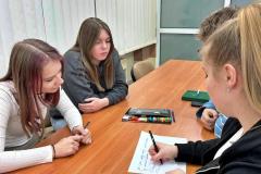 Grupa wychowanków pracuje wspólnie przy stole, zapisując notatki na kartce.