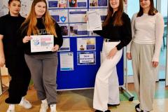 Grupa wychowanków stoi przy wystawie przygotowanej z okazji „Dnia Bezpiecznego Internetu”.