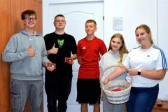 Pięcioro uśmiechniętych wychowanków na tle białej ściany. Dziewczyna trzyma koszyk ze słodkościami.