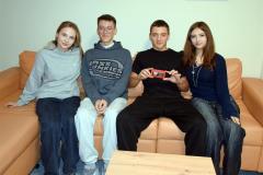 Czworo uśmiechniętych wychowanków siedzi na brązowej kanapie. Jeden z nich trzyma czekoladkę wręczoną z okazji Dnia Chłopaka.