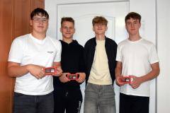 Czworo uśmiechniętych wychowanków pozuje na tle ściany. Troje z nich trzyma w ręku czekoladkę wręczoną z okazji Dnia Chłopaka.