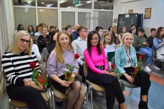 Pierwszy rząd zajmują wychowawcy Bursy Regionalnej w Ostrołęce, każdy z nich trzyma czerwoną różę otrzymaną podczas uroczystości z okazji Dnia Edukacji Narodowej. W tle widoczni są wychowankowie i inni uczestnicy wydarzenia.