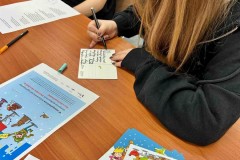 Młodzież pisze życzenia na kartkach. Na stole znajdują się materiały potrzebne do zajęć