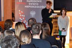 Młodzież w skupieniu prowadzi wieczór patriotyczny, w tle tablica z napisem 11 listopada, Narodowe Święto Niepodległości, Białym Orłem i liśćmi w kolorze biało czerwonym, z przodu widać siedzącą młodzież.