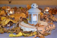 Dekoracje w postaci liści jesiennych, wśród których stoją zapalone lampiony.