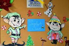 Świąteczna gazetka, na której znajdują się dwa kolorowe elfy wykonane z papieru. Pośrodku umieszczono biały napis „Wesołych Świąt” na niebieskim tle. Całość uzupełniają barwne dekoracje świąteczne wykonane przez młodzież, a w górnej części gazetki widnieje kolorowy logotyp Bursy