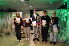 Pięcioro wychowanków Bursy Regionalnej w Ostrołęce stoi w rzędzie . W rękach trzymają różnokolorowe palmy wielkanocne (kurpiowskie) oraz dyplomy za udział w III międzyinternackim konkursie plastycznym na „Palmę Wielkanocną”. Za nimi znajduje się po obu stronach płótno z namalowanymi ozdobami wiosenno-wielkanocnymi: kolorowe pisanki, kwiaty, zajączki, bazie).