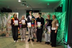 Pięcioro wychowanków Bursy Regionalnej w Ostrołęce oraz opiekun koła artystycznego stoi w rzędzie. Wychowankowie w rękach trzymają różnokolorowe palmy wielkanocne (kurpiowskie) oraz dyplomy za udział w III międzyinternackim konkursie plastycznym na „Palmę Wielkanocną”. Za nimi znajduje się po obu stronach płótno z namalowanymi ozdobami wiosenno-wielkanocnymi: kolorowe pisanki, kwiaty, zajączki, bazie).