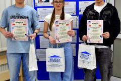 Troje wychowanków stoi przy tablicy na której znajduje się napis: 21 lutego Międzynarodowy Dzień Języka Ojczystego. W rękach trzymają dyplomy i nagrody rzeczowe.