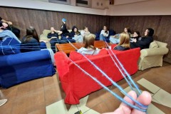 Młodzież zgromadzona na kanapach wokół stolia przekazuje sobie kłębek nici tworząc w ten sposób sieć powiązań - więzy