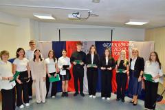 Młodzież wraz z wychowawcami podczas uroczystości z okazji Dnia Edukacji Narodowej pozują na tle okolicznościowej dekoracji