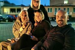 Uśmiechnięci wychowawcy siedzą na ławce. W tle widać budynek bursy. 