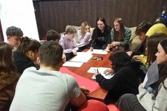 Wychowankowie tworzą plakaty potrzebne do zajęć. Na stole znajdują się arkusze papieru i mazaki.