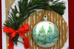 Kartka świąteczna na której znajduje się biała wypukła bombka, na której namalowane są zielone choinki. Wokół bombki są okręgi: beżowy i biały. Na białym okręgu wywinięta jest zielona gałązka z czerwoną kokardką i białymi perełkami. W lewym górnym rogu znajduje się napis: Wesołych Świąt. Pod kartką znajduje się napis: III miejsce: Mąka Magdalena – Internat I LO im. gen. Józefa Bema w Ostrołęce