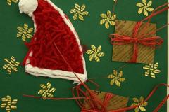 Kartka świąteczna: Na żółtym kartonie przyklejona  jest zielona kartka na której znajduje się biało – czerwona czapka Mikołaja, dwa prezenty obwiązane czerwoną wstążką, złote gwiazdki. Na górze na czerwonym pasku znajduje się napis Wesołych świąt. Pod kartką znajduje się napis: Wyróżnienie: Samsel Szymon – Internat przy ZSZ nr 1 w Ostrołęce