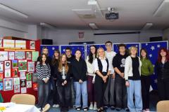 Na zdjęciu znajdują uczestnicy (wychowankowie Bursy Regionalnej w Ostrołęce),  XIII Międzyinternackiego konkursu plastycznego na „Kartkę Bożonarodzeniową” wraz z opiekunem koła artystycznego. Z tyłu znajduje się czerwona tablica z kartkami konkursowymi i niebieska tablica z migającymi światełkami  i białymi gwiazdkami.