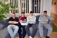 Czworo uśmiechniętych chłopców pozuje z koszykiem czekoladek siedząc na kanapie