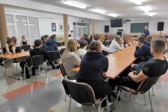 Wychowankowie siedzą przy stolikach i słuchają wykładu policjanta.