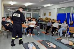 Wychowankowie siedzący na krzesłach oraz słuchający Strażaka, na podłodze leżące fantomy