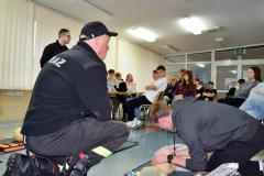 Wychowanek ćwiczący resuscytacje na fantomie, obok kucający Strażak