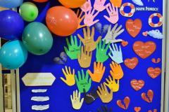 Na zdjęciu widać wystawę prac wychowanków, poświęconą depresji (napis: „Międzynarodowy Dzień Depresji”). Tablica jest ozdobiona kolorowymi wycięciami w kształcie dłoni z nazwami emocji (np. smutek, lęk, samotność), sercami oraz rysunkami chmur i słońca. Po lewej stronie znajdują się kolorowe balony z imionami.