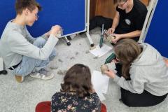 Wychowankowie siedzący na podłodze kleją sznurek na słoiki