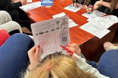 Młode osoby biorą udział w zajęciach związanych ze Światowym Dniem Wody. Pracują nad kartami edukacyjnymi, rozwiązując wykreślanki i zadania dotyczące tematu wody. Na stole widoczne są materiały edukacyjne oraz plansza z logo akcji 