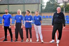 Uśmiechnięci członkowie drużyny wychowawców pozują na boisku po zakończonym meczu piłki siatkowej.