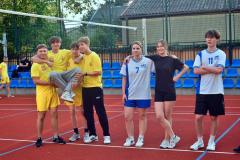 Uśmiechnięci członkowie drużyny wychowanków pozują na boisku po zakończonym meczu piłki siatkowej.