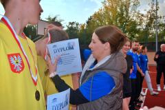 Wręczenie dyplomu. Pani Dyrektor trzyma w rękach dyplom i nakłada medal na szyję osoby stojącej przed nią.