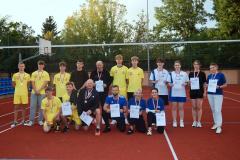 Grupowe ujęcie wszystkich uczestników turnieju sportowego. Mają w rękach dyplomy, na szyjach medale. 