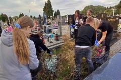 Wychowankowie wraz z wychowawcą sprzątają zaniedbany grób