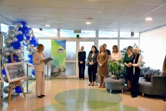 Uroczyste wydarzenie w Bursie Regionalnej w Ostrołęce. Kilka osób stoi na tle ozdób balonowych i baneru bursy, a jedna z nich, trzymając dokumenty, przemawia do zebranych.