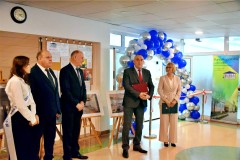 Grupa osób uczestniczących w otwarciu stołówki na tle łuku z balonów i wstęgi. Jedna z osób przemawia do zgromadzonych gości.