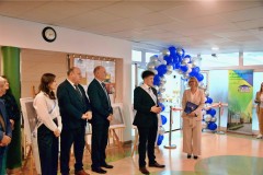 Kontynuacja  uroczystości w Bursie Regionalnej w Ostrołęce. Grupa osób, w tym młodzież i dorośli, stoi w eleganckich strojach, a jedna z osób, przedstawiciel młodzieży, zabiera głos.
