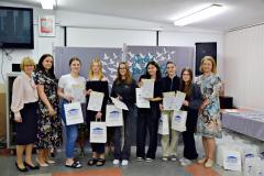 Pani Dyrektor, wychowawcy oraz nagrodzone wychowanki z dyplomami i nagrodami w ręku  pozują do zdjęcia na tle dekoracji.