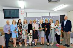Pani Dyrektor oraz Rada Pedagogiczna pozują do zdjęcia trzymając w ręku czerwoną różę.