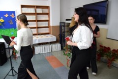 Młodzież, która idzie wręczyć  kadrze pedagogicznej kwiat czerwonej róży