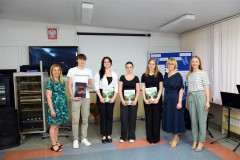 Pani dyrektor, wychowawcy stoją uśmiechnięci wraz z nagrodzonymi wychowankami trzymającymi w ręku nagrody książkowe,  w tle dekoracji do zakończenia roku szkolnego w bursie