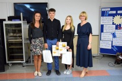 Pani dyrektor, wychowawca z wychowankami trzymających w ręku nagrody i dyplomy, w tle dekoracji do zakończenia roku szkolnego w bursie