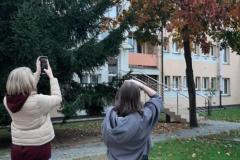 Dwie wychowanki stoją z boku budynku bursy i wykonują zdjęcie przyrody i budynku bursy