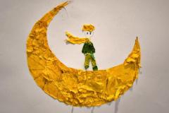 Na zdjęciu widać chłopca stojącego na księżycu z powiewającym szalikiem, wykonanego z żółtych liści