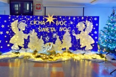 Niebieska tablica na której znajdują się: wycięte z papieru białe gwiazdki, 2 białe anioły, lampki, 4 białe choinki. Pośrodku w drewnianym żłóbku leży postać Jezusa. Na tablicy znajduje się napis: Cicha noc, święta noc. Nad nim wisi biała duża gwiazda. Na podłodze znajduje się biała tkanina, na której leżą zapalone lampki. Z boku stoi zielona choinka udekorowana bombkami.