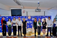 Na pierwszym planie stoi 12 osób: wychowankowie bursy i wychowawcy bursy. Ubrani odświętnie w biało – czarne stroje. Na głowie 5 osób znajdują się czapki Mikołaja. W rękach trzymają mikrofony i podkładki ze scenariuszami uroczystości. Za nimi znajduje się niebieska tablica na której znajdują się: wycięte z papieru białe gwiazdki, 2 białe anioły, lampki, 4 białe choinki. Pośrodku w drewnianym żłóbku leży postać Jezusa. Na tablicy znajduje się napis: Cicha noc, święta noc. Nad nim wisi biała duża gwiazda. Na podłodze znajduje się biała tkanina, na której leżą zapalone lampki. Z boku stoi zielona choinka udekorowana bombkami.