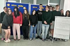 Wychowankowie bursy stoją razem przy dekoracji związanej z kalamburami. Wspólne zdjęcie pokazuje dobrą zabawę i integrację młodzieży