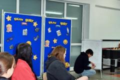 Wychowankowie bursy podczas wspólnej zabawy w kalambury. Jedna z osób rysuje hasło na tablicy, a pozostali próbują je odgadnąć. Spotkanie przebiega w miłej i integracyjnej atmosferze